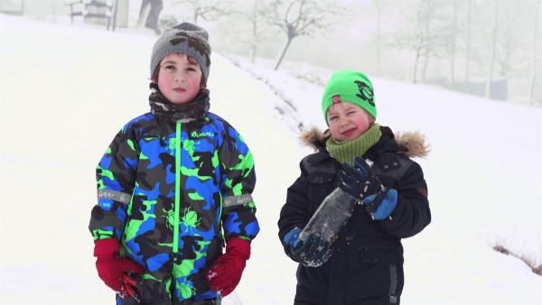Zwei Jungs in Winterbekleidung stehen vor einer Schneelandschaft.