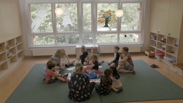 Ein Mädchen sitzt mit anderen Kindern im Kreis auf dem Boden. Sie gucken sich neugierig Bilder an.