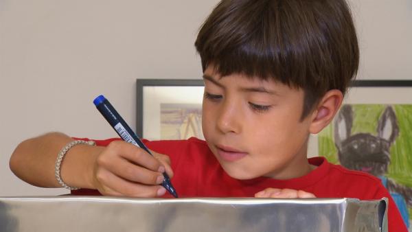 Ein Vorschulkind malt konzentriert mit einem blauen Stift auf eine Silberfolie.
