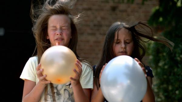 Amia und Hannah pusten sich mit Ballons Luft in die Gesichter.