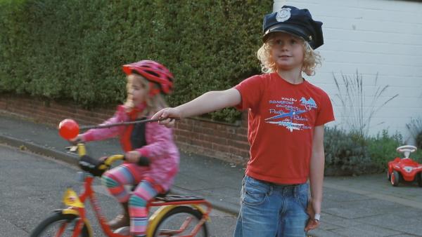 Ein Kind mit einer Polizeimütze und einem selbstgebastelten Anhaltestab steht auf der Straße.