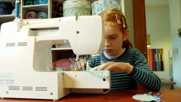 Ein Mädchen mit Sommersprossen  und Tierhaarspangen benutzt konzentriert eine Nähmaschine.