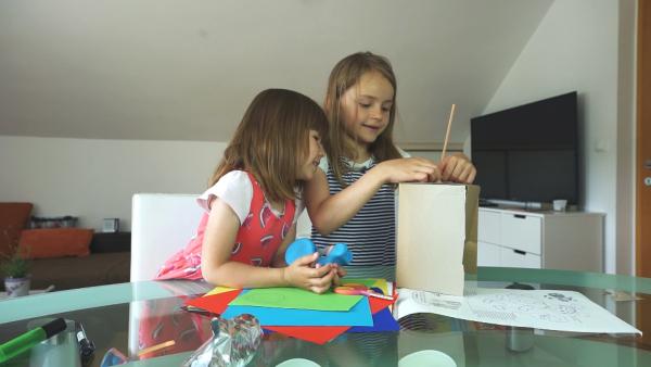 Zwei Vorschulkinder sitzen an einem Tisch mit Bastelutensilien und beugen sich über einen Karton.