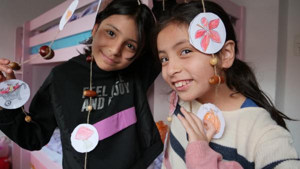 Zwei Mädchen zeigen ihre selbst gebastelte Girlande aus Eicheln, Perlen und Herbstbildern.