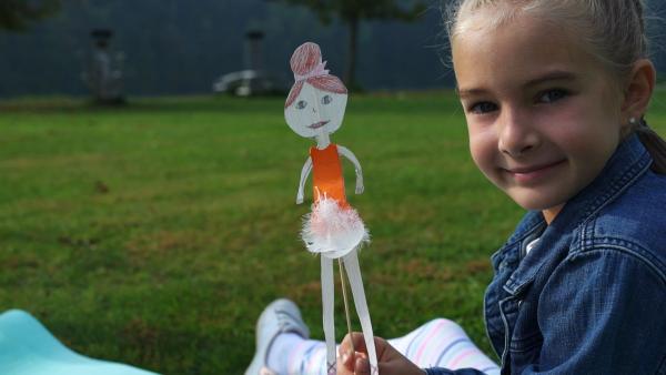 Ein Mädchen hält eine Ballerina aus Papier in die Kamera.