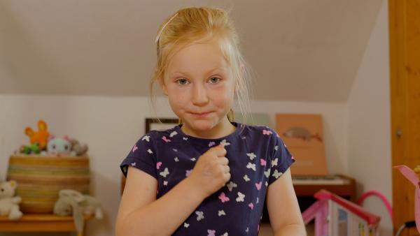 Ein Mädchen hält ihre geballte Hand vor den Oberköper und blickt in die Kamera.