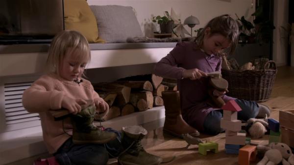 Zwei Mädchen sitzen nebeneinander auf dem Wohnzimmerboden und putzen je einen Schuh mit einer Bürste.