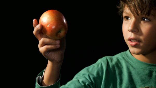 Ein Junge hält einen roten Apfel vor sich. Er trägt ein grünes Shirt.