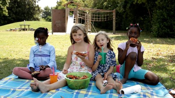 Vier Mädchen sitzen auf einer Picknickdecke im Park und essen Pizza.