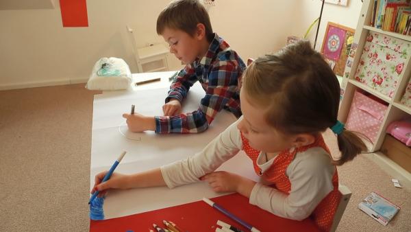 Ein Junge und ein Mädchen sitzen an einem Tisch im Kinderzimmer. Sie malen gemeinsam ein Bild.