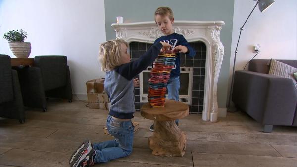 Zwei Jungs stapeln Bausteine auf einem Holztisch immer höher. Konzentriert bauen sie einen Turm.