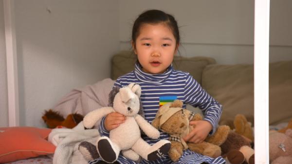 Ein Mädchen sitzt in ihrem Bett mit zwei flauschigen Kuscheltieren in der Hand.