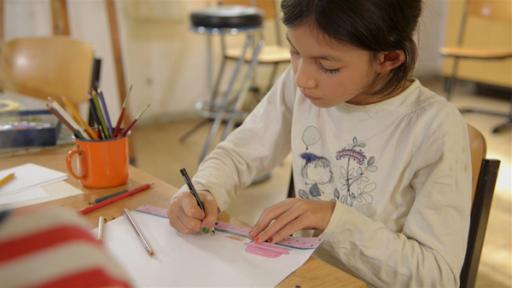 Rechte: KiKA/Motion Works GmbH Ein Mädchen sitzt an einem Schreibtisch und hält einen Stift über einem weißen Blatt Papier.