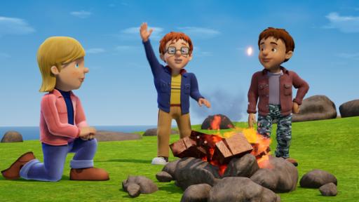 Zwei Jungs und ein Mädchen an einem Lagerfeuer, das von Steinen umgeben ist. Im Hintergrund das Meer.
