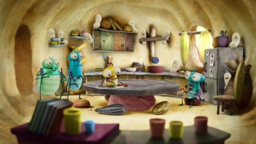 Madensitting | Rechte: ©Aardman Animations 2022 Im Inneren eines Apfels - in der Küche von Floyds Wohnung - sitzt Floyd mit einem Comic in den Händen am Esstisch und schaut unglücklich zu seinen Eltern, die in der Nähe der Türe stehen. Auf dem Küchentisch sitzt PB, Floyds jüngere Schwester, mit einem Stift in der Hand und einem Zettel vor sich.