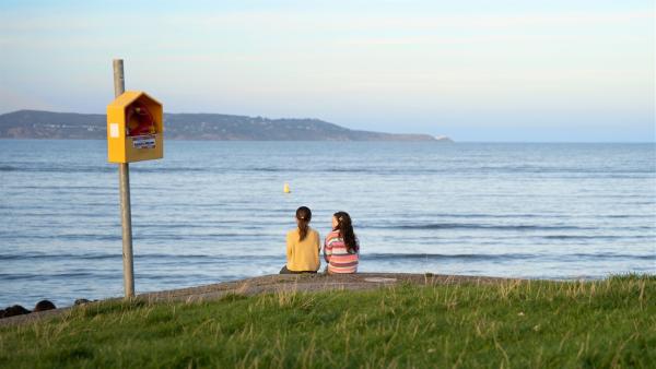 Yana und Chloe sitzen am Ufer und schauen auf das Meer.