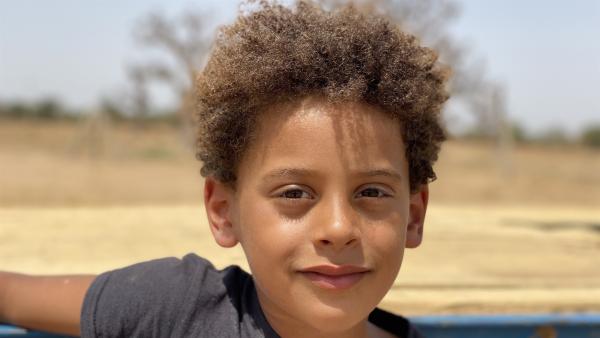 Der Junge Lamine im Portrait. Er trägt ein dunkelgraues T-Shirt und hat braune, lockige Haare.