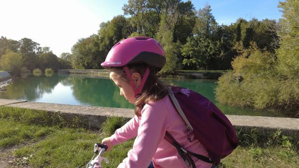 Nika fährt mit dem Fahrrad am Ufer eines Flusses entlang.