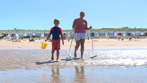 Rechte: ZDF/KRO-NCRV Hugo steht mit seiner Mutter am Strand. Sie sind mit Eimer und Netzen ausgerüstet. Im Hintergrund sind Strandhäuser zu sehen.