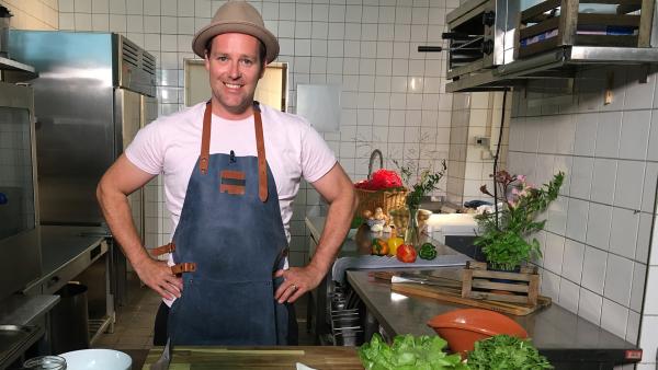 Ben steht in seiner Küche mit Kochschürze, bereit zum Kochen.