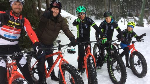Ben, zweiter von links, sitzt auf einem Fahrrad, einem Fatbike.  Vor ihm sitzt einer, hinter ihm sitzen drei Extremsportler ebenfalls auf Fatbikes. Sie stehen im Schnee.