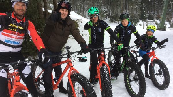Ben, zweiter von links, sitzt auf einem Fahrrad, einem Fatbike.  Vor ihm sitzt einer, hinter ihm sitzen drei Extremsportler ebenfalls auf Fatbikes. Sie stehen im Schnee.
