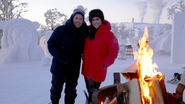 In der Mitte stehen Ben und Jess. Im Vordergrund brennt ein Lagerfeuer. Im Hintergrund sind eindrucksvolle Eisfiguren zu sehen.