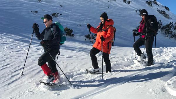 Im Schnee gehen hintereinander von links nach recht Ben, Jess und Bergführerin Susanne. Sie tragen Schneeschuhe.