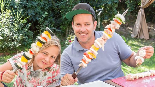 Ben und Ole sitzen am Tisch und zeigen ihre großen Grillspieße. 