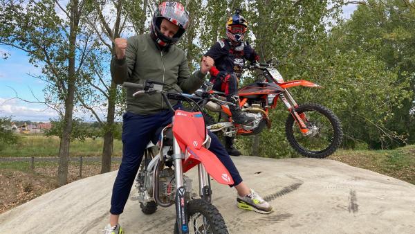 Auf einem kleinen Hügel sitzt Ben auf einem Motocross und trägt ein Helm. Hinter ihm sitzt Luc Ackermann ebenefalls auf einem Motocross. Er trägt sowohl Helm als auch einen Motocross-Anzug.