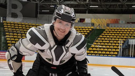 Auf der Eisfläche eines Eishockey-Stadions stehen Ben (links) und Lola. Sie tragen Eishockey-Ausrüstung, einen Helm und halten Hockey-Schläger in den Händen.