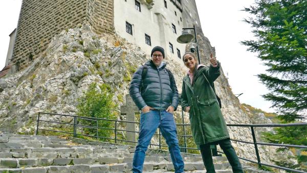 Ben und Jess stehen unterhalb des Dracula-Schlosses Bran. Sie lächeln in die Kamera, während Jess den Daumen nach oben zeigt.