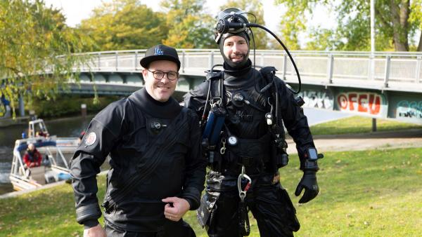 Ben steht neben einem Taucher der Polizei Hamburg. Im Hintergrund eine Brücke.