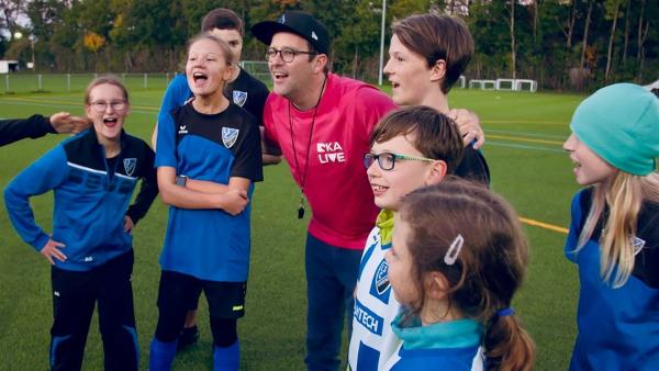 Ben steht auf einem Fußballfeld zwischen Spielerinnen und Spielern der Inklusionsmannschaft des 1.SC Gröbenzell.