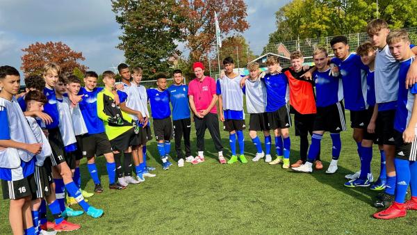 Ben besucht den SV Curslack-Neuengamme, einem Fußballverein. Die Mannschaft steht im Halbkreis, Ben in der Mitte. Dabei hat er seine rote Mütze auf.