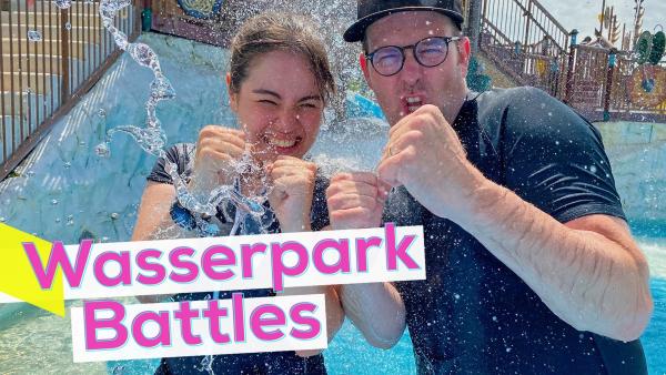 Sarah und Ben stehen am Rand eines Schwimmbeckens und werden von Wasser bespritzt. Links steht Wasserpark Battles in pinker Schrift auf weißem Grund.