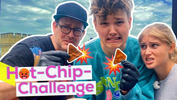 Eine Fotomontage. Links steht in pinken, fetten Buchstaben: "Hot-Chip-Challenge". Das "O" im Schriftzug ist mit einem roten, schwitzendem Emoji ersetzt. Mit Handschuhen halten HeyMoritz und Ben zwei sehr scharfe Chips vor die Kamera. Zoe sieht besorgt aus.