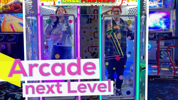 Sarah und Ben in einer bunten Arcade-Halle. Beide stehen jeweils in einer Röhre des Ball Madness-Spielautomaten. Unten die Aufschrift: Arcade next Level.