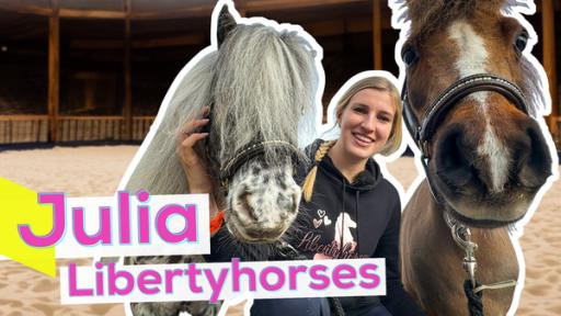 Rechte: KiKA/Andrea Thoben Influencerin Julia hockt auf Sandboden in einer Reithalle. Links dicht neben ihr der Kopf des Ponys Duke und rechts der große Braune Paquito. Aufschrift: Julia Libertyhorses.
