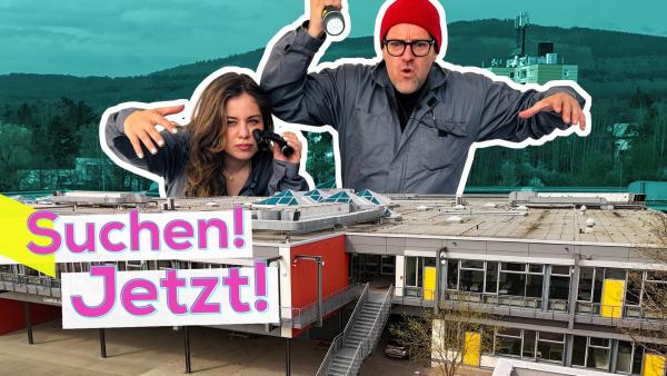 Ben und Sarah in Übergröße hinter dem Gebäude der Altkönigschule Kronberg. Sarah hält ein Fernglas und Ben eine Taschenlampe in der Hand. Aufschrift unten links: Suchen! Jetzt!