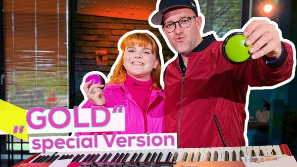 Musikerin LOI (links) und Ben (rechts) stehen hinter einem E-Piano. Beide sind fröhlich und halten jeweils einen kleinen Buzzer in der Hand. Aufschrift: „Gold“ special Version.