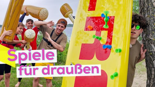 Linke Bildhälfte: Lukas und das DLRG-Team mit aufblasbaren Keulen in Holzoptik. Rechte Bildhälfte: Lukas hinter einem Surfboard. Auf dem Board und auf seiner Sonnenbrille kleben Dartpfeile aus Silikon. Aufschrift: Spiele für draußen.