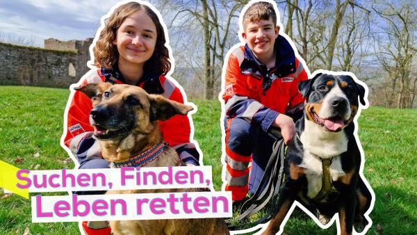 Magdalena und Matthias hocken in Arbeitsuniform der Rettungshundestaffel auf einer Wiese mit ihren Spürhunden Henry und Hope. Aufschrift: Suchen, Finden, Leben retten.