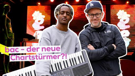 Rechte: KiKA/Filip Felix Musiker Samuel aka bac mit Keyboard unterm Arm vor seiner Bühne in Köln. Eng neben ihm Ben gut gelaunt. Aufschrift: bac - der neue Chartstürmer?!