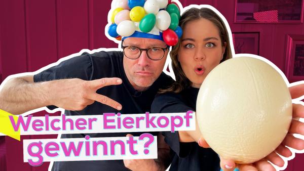 Links Ben mit einer Badekappe an der viele Eier aus Plastik kleben. Rechts dicht neben ihm Sarah mit erstauntem Gesichtsausdruck. Sie hält ein Straußen-Ei in die Kamera. Aufschrift: Welcher Eierkopf gewinnt?