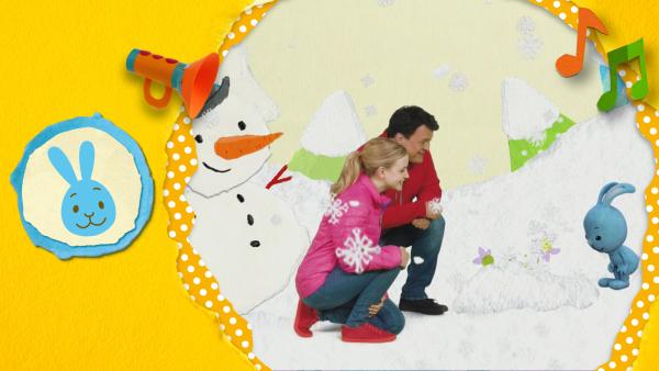 Kikaninchen, Anni und Christian betrachten die ersten Frühblüher, die aus einem Schneehäufchen hervorschauen. Im Hintergrund ein Schneemann.