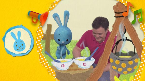 Christian und Kikaninchen kochen mit Karotten, Zwiebeln und Lauch eine leckere Suppe über einer Feuerstelle. 