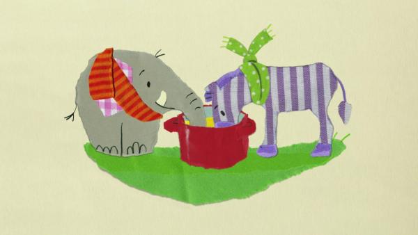 Ein Elefant und eine Zebra fressen aus einem Topf.