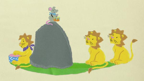 Eine Maus trommelt auf einem Felsen, während drei Löwen aufmerksam zuschauen.