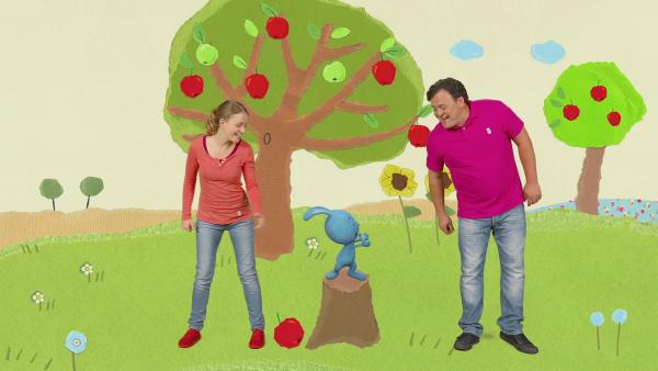 Anni, KiKANiNCHEN und Christian stehen auf einer Wiese. Im Hintergrund 2 große Apfelbäume.
